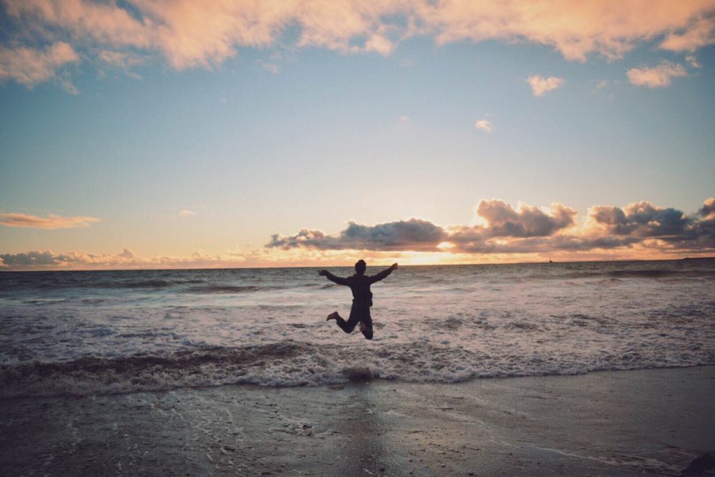 pexels photo 59028 59028 A person joyfully jumps on the shore with a stunning ocean sunset as the backdrop.