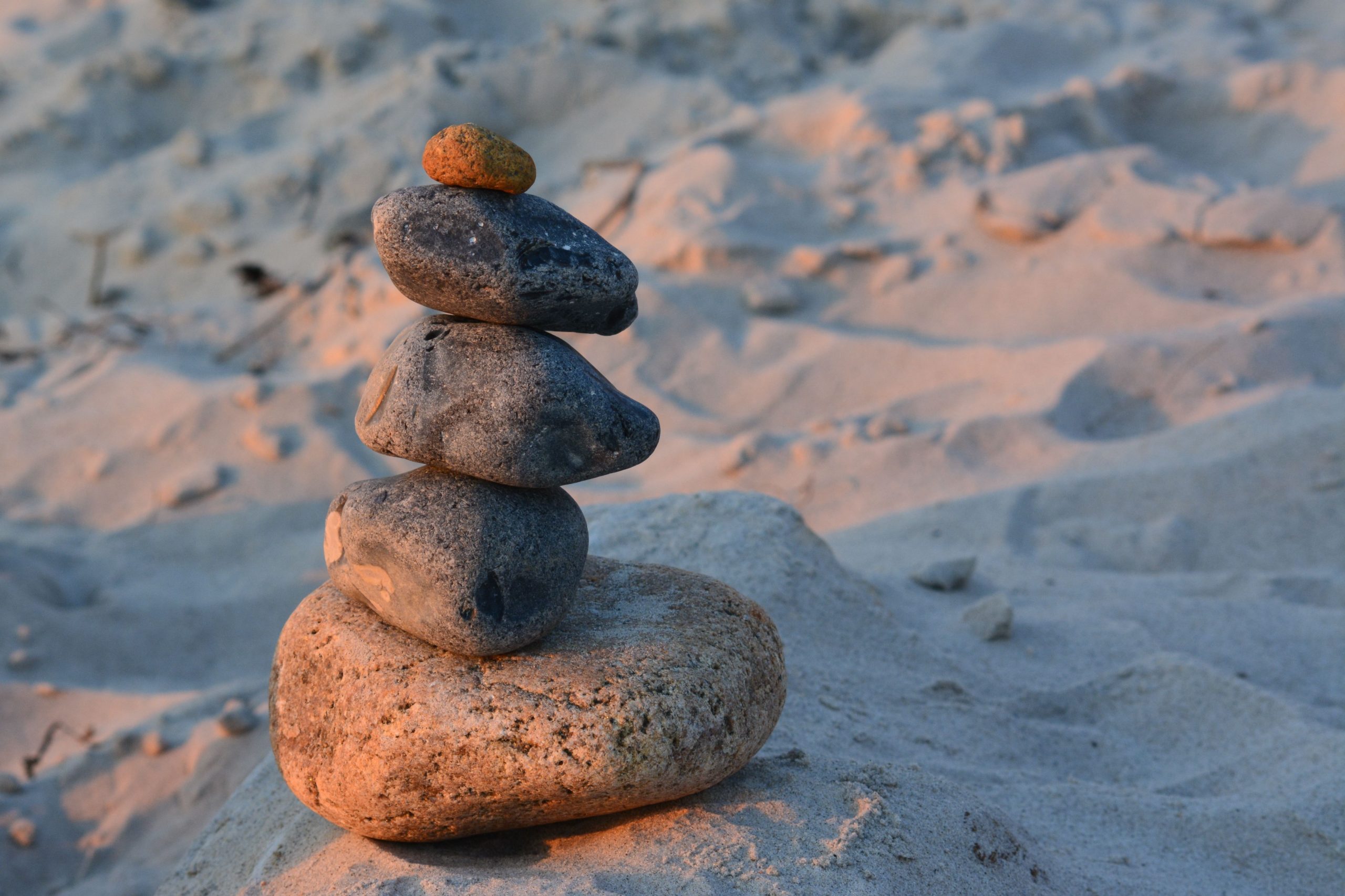 Bilan de compétences à Cestas Close-up of a balanced stone cairn on a sandy beach with warm sunset lighting.