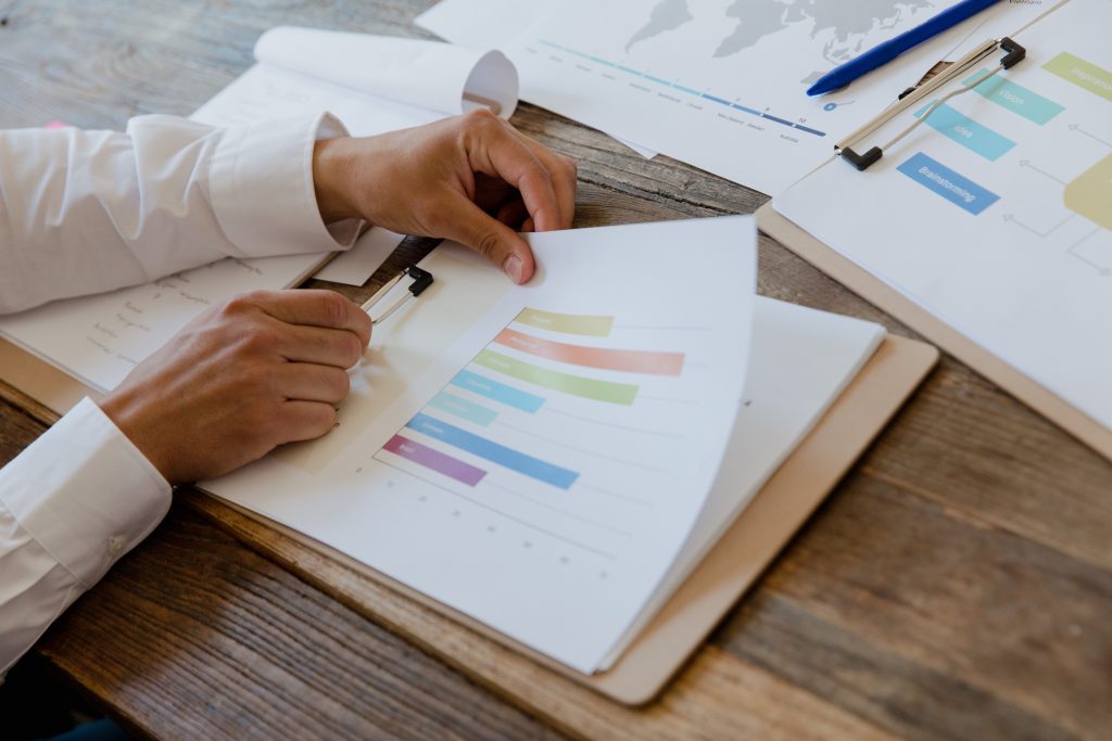 Entreprises Close-up of hands reviewing business report with colorful charts and graphs on a wooden desk.